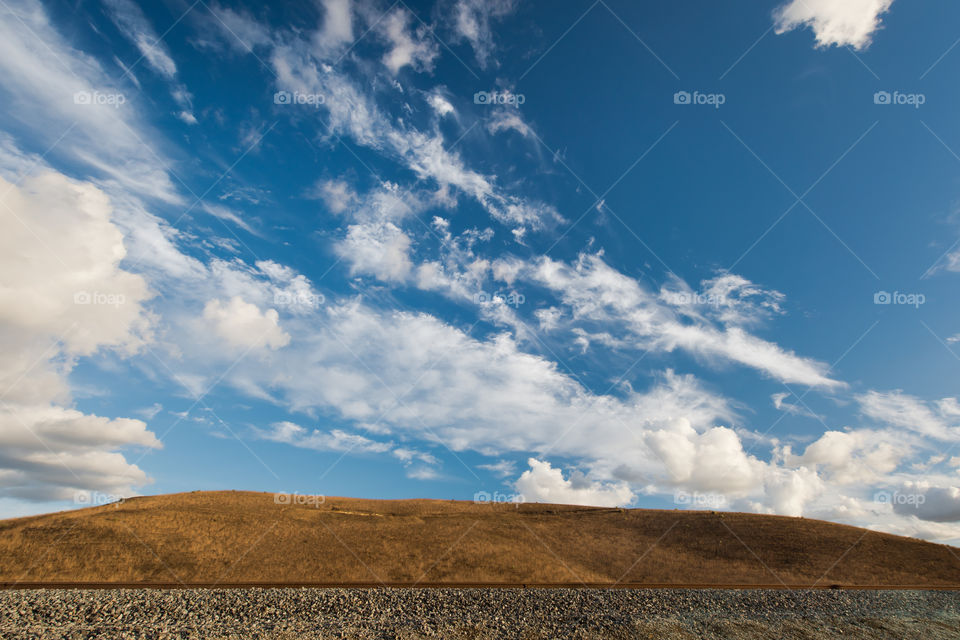 Railroad track an empty brown hill and a beautiful cloudy sky