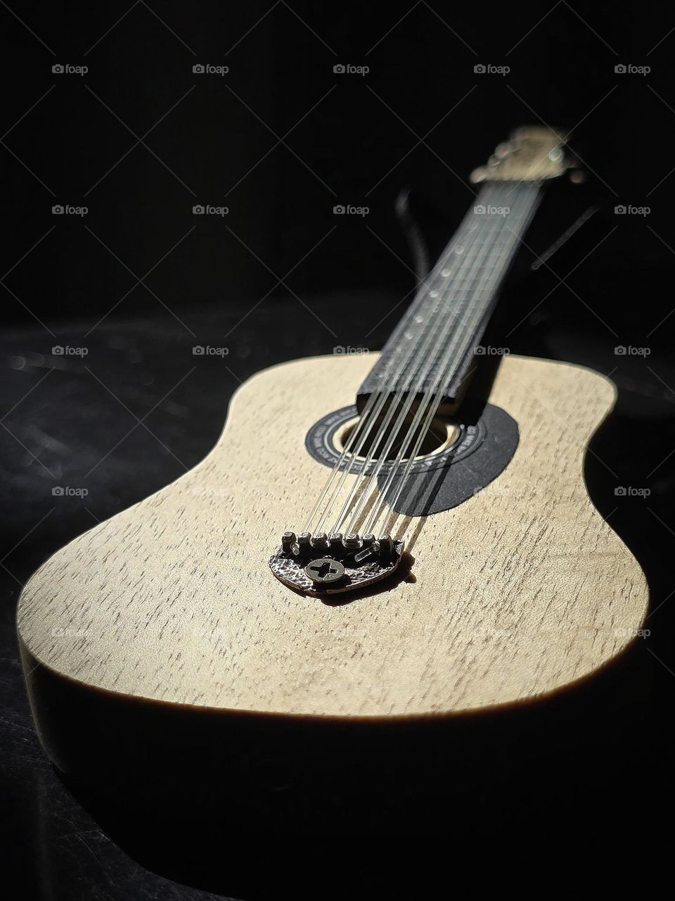 Small collection guitar placed on a table with dark background while receiving sunlight on it.