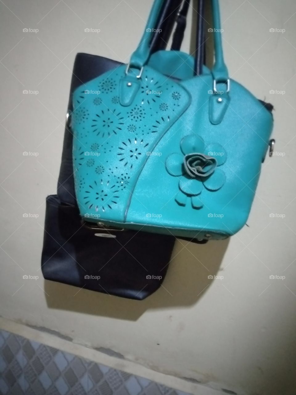 bags hangs on the wall, the bags are made up of sea green and black colours. they bags are casting shadows on the wall.