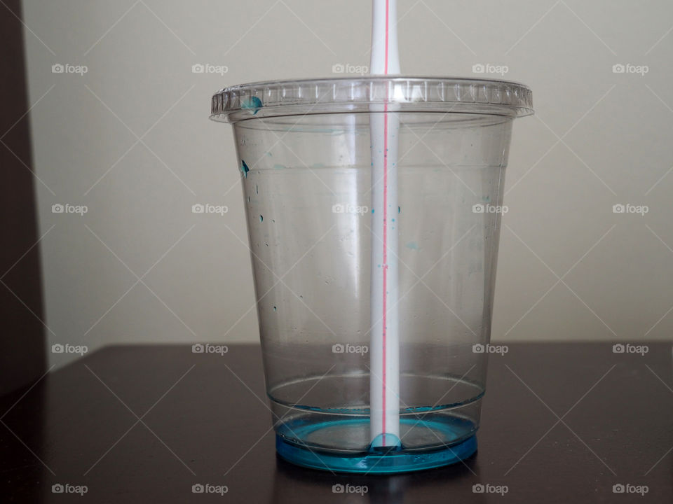 Tasty Beverage. Disposable clear plastic cup with straw with only a few blue drops in cup