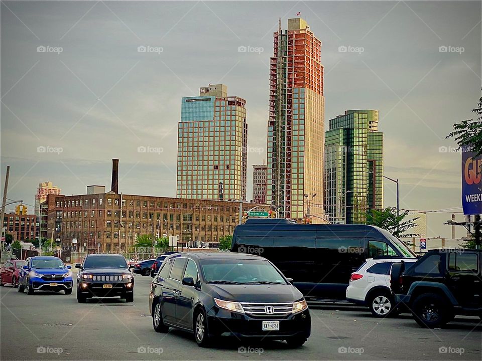 Cars are driving down „Borden Ave“ onto „Vernon Jackson Ave“ by the „East River“ at „Newtown Creek“ by the „Pulaski Bridge“ incessantly. The sun is just about to set behind the horizon at twilight time. 2022. Hypnotic Productions