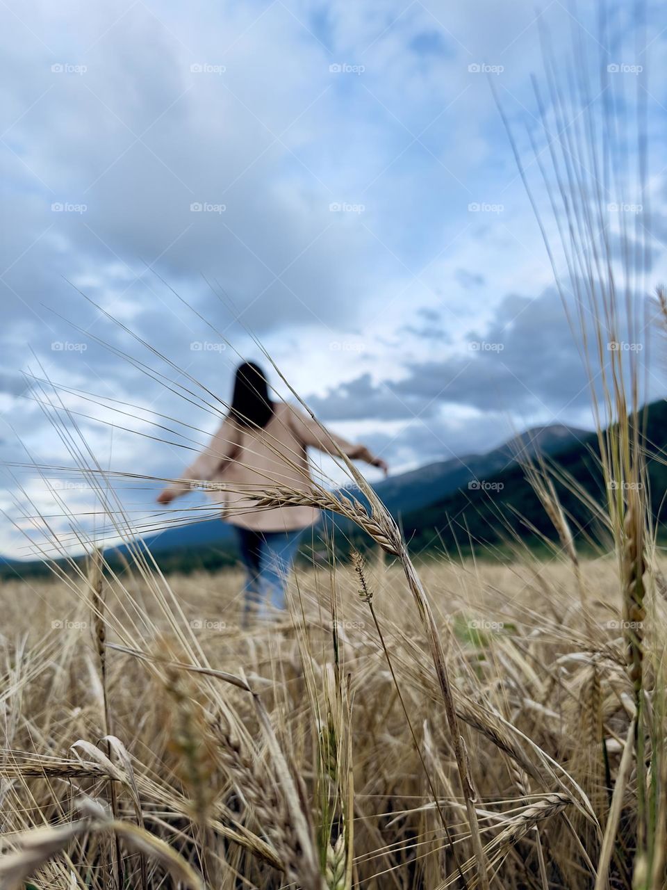 a girl in a beige shirt walks through a wheat field