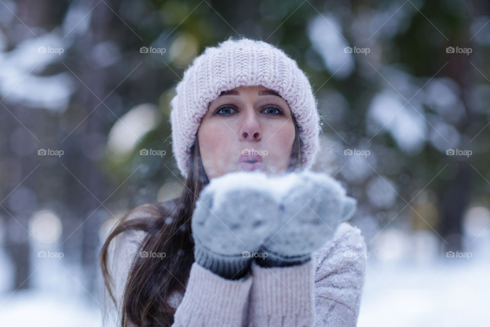 Young Caucasian woman blowing snow at winter forest 