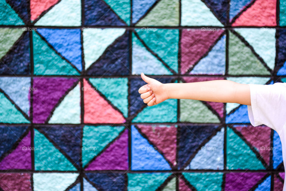 Person's arm giving a thumbs up against a colorful, bright, triangular patterned concrete wall