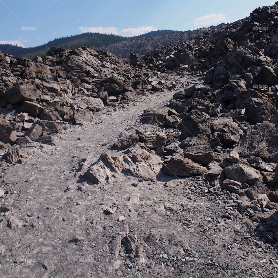 A path leading through hills of Obsidian show off the geological beauty of Central Oregon on a sunny day. 