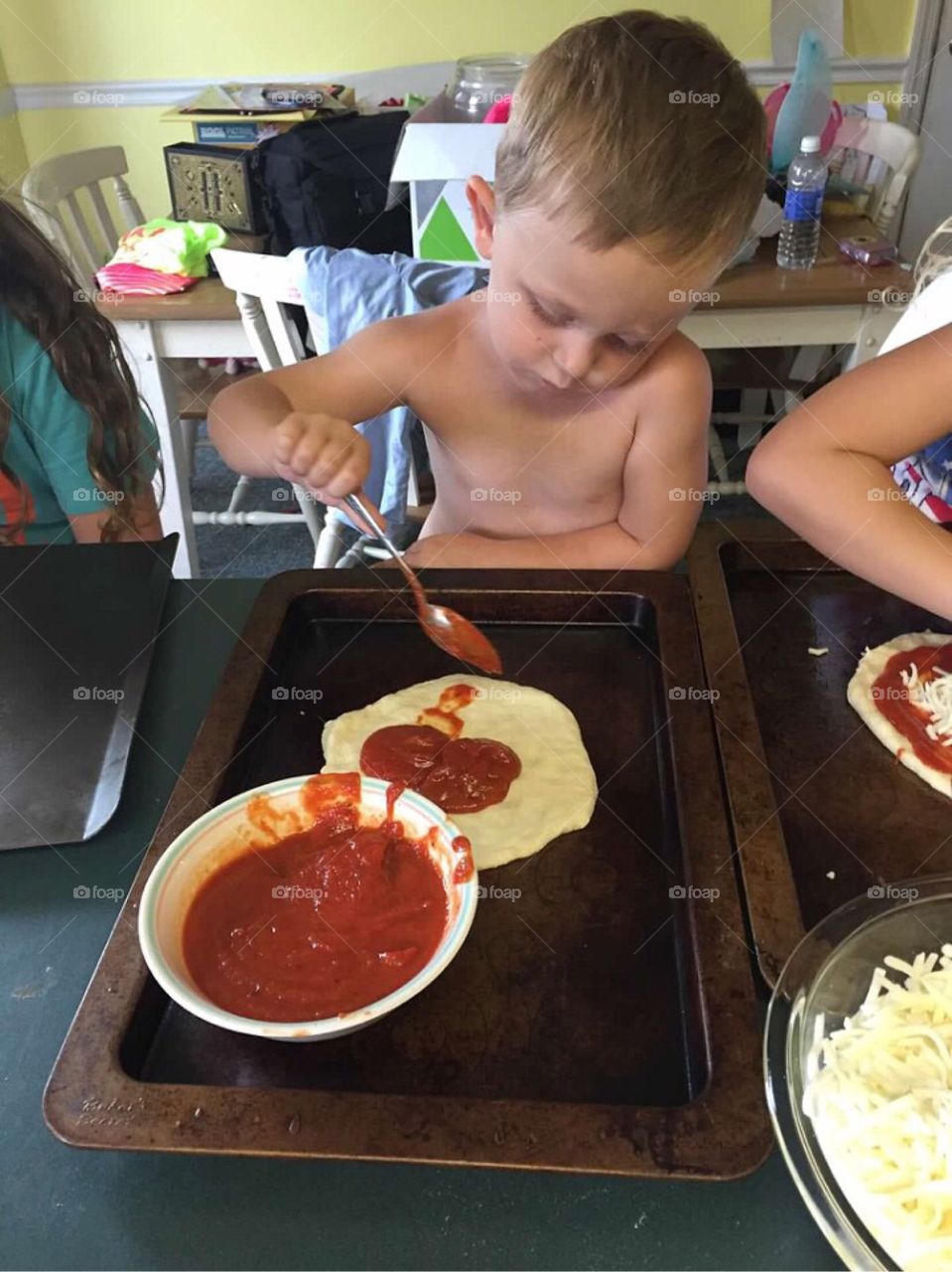 Little boy adding sauce to his pizza. 