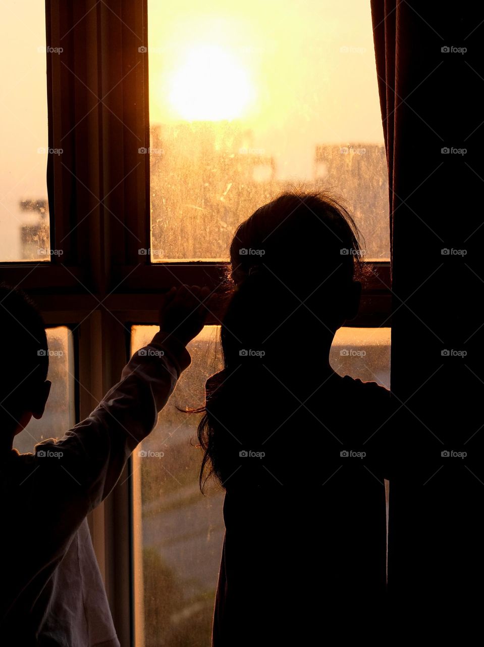 Two children are looking at the sunrise in the morning at the window