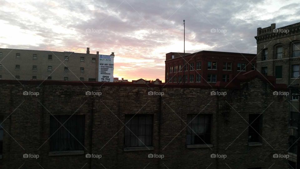 City scape at dusk. Brick building foreground with sunset background.