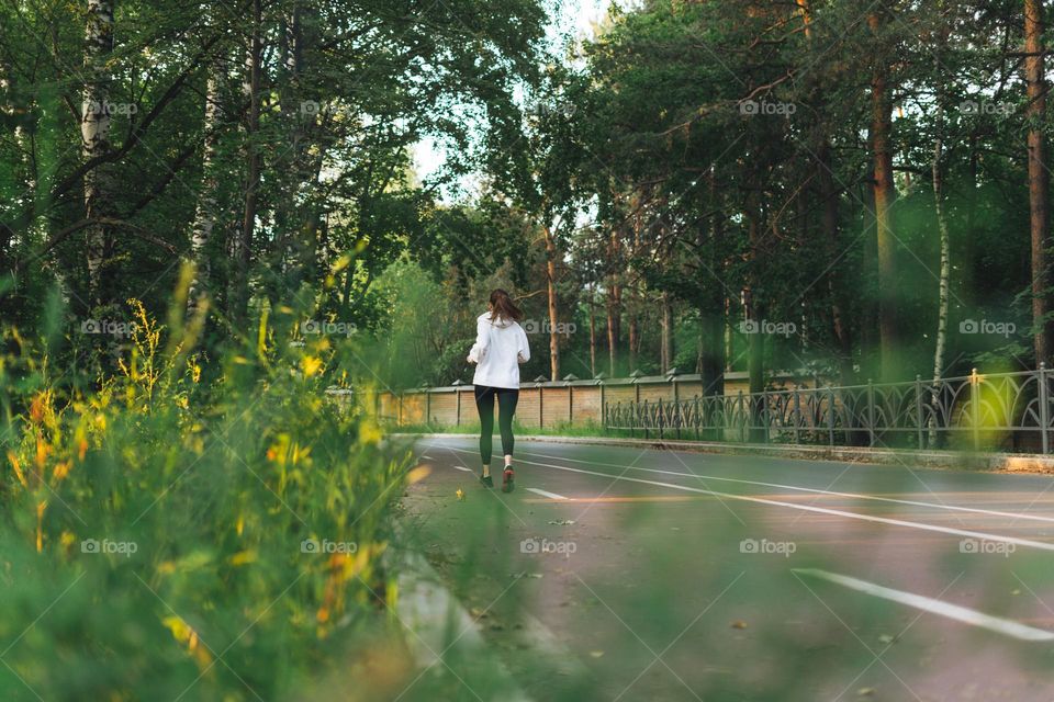 Young slim woman brunette in sport clothes running at autumn park on golden hour sunrise time. Health and wellness, fitness lifestyle