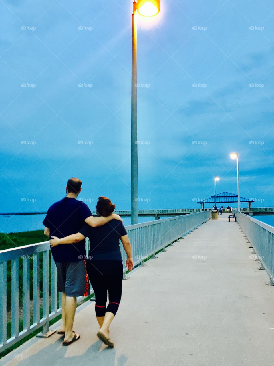 Average couple taking a romantic walk on a dock at sunset