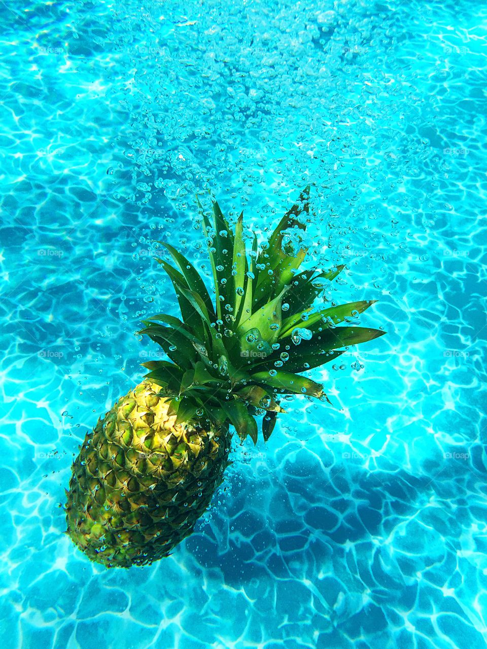 Pineapple fruit sinking under water in a swimming pool. 