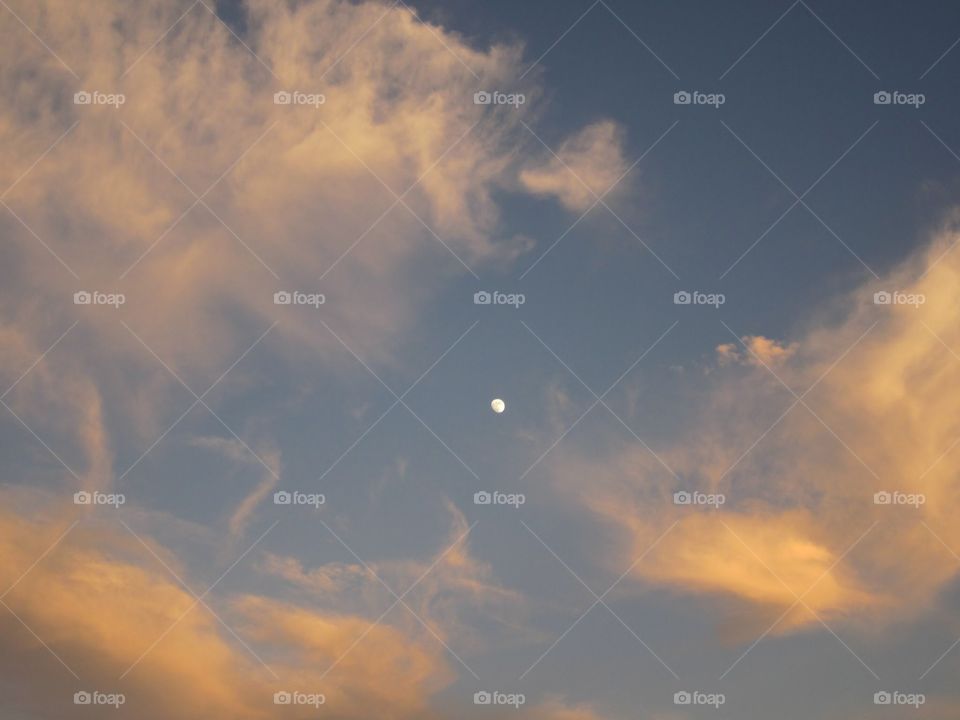 Small moon in sky with clouds at sunrise.