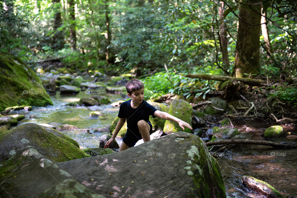 Young boy hiking and climbing over a rock in a stream 