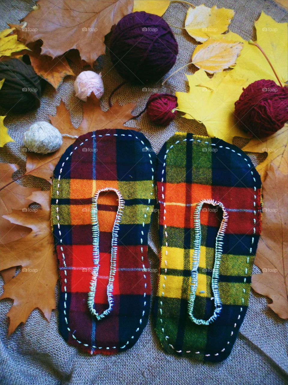 warm homemade slippers with their hands on the background of autumn leaves