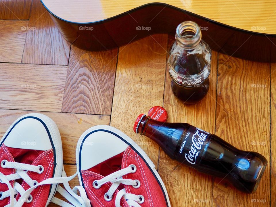 Coca Cola bottles on hardwood floor with red sneakers and guitar.