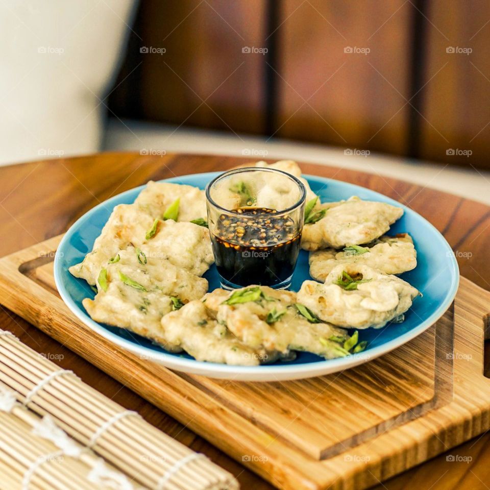 Fried tempeh sprinkled with chopped green onions c ombined with soy sauce sauce. Plate. Tempeh. Glass. Table. Wood. Wood motif. Café. Cutting board. Snack. Eat. Food. Fried food. Crispy. Photography.