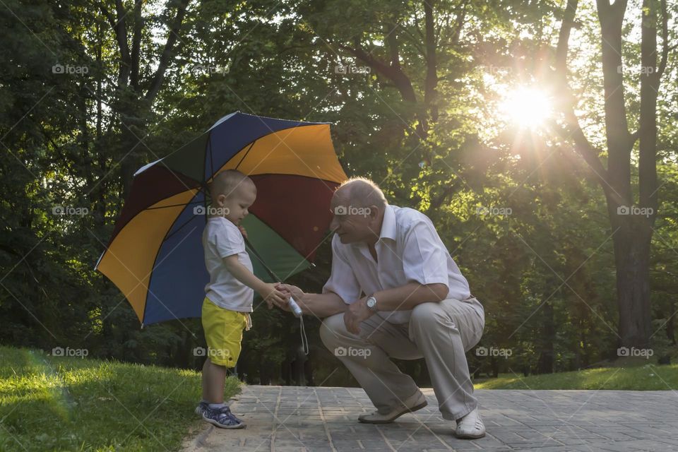 An old grandfather with his grandson walk together in the park at the weekend and play under an umbrella.