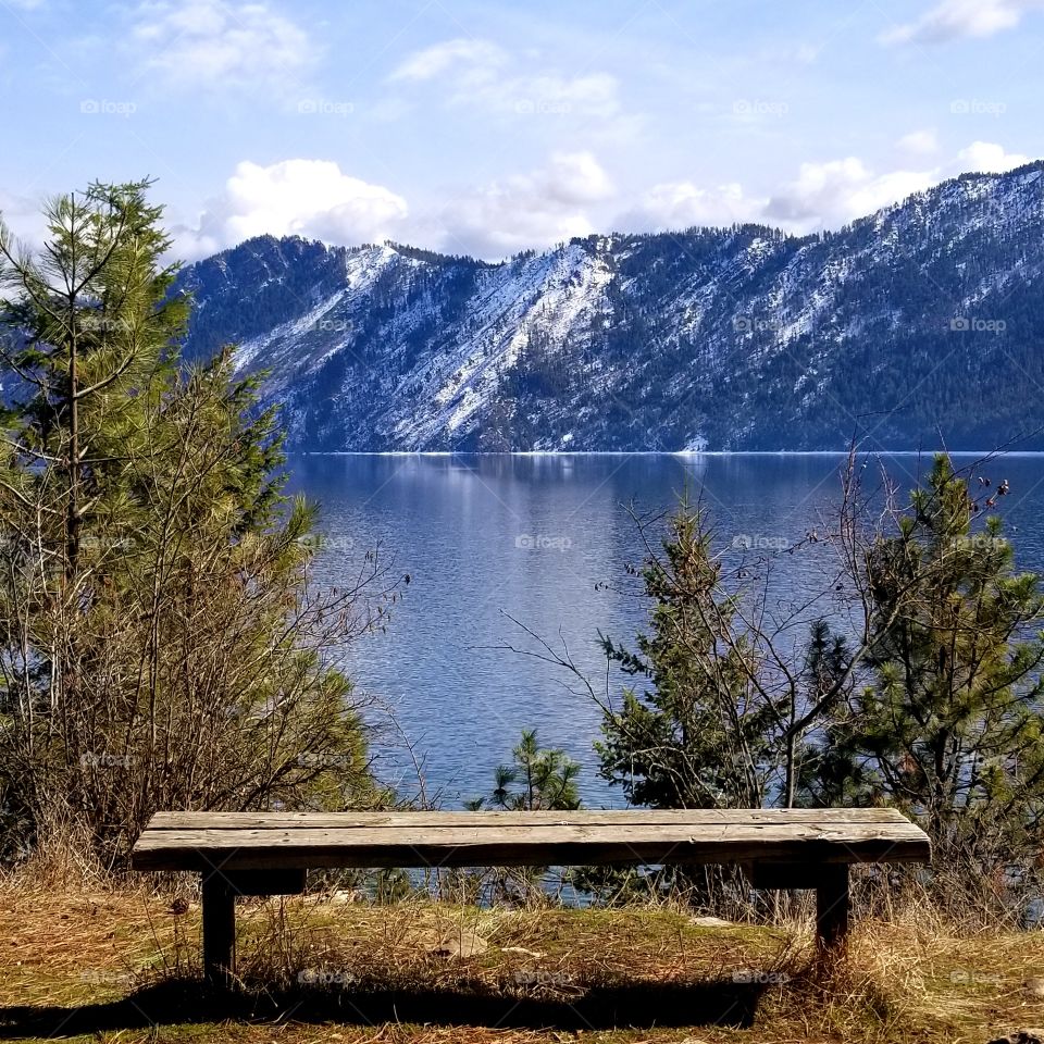 wooden bench with a reflection of mountain ridge on the lake