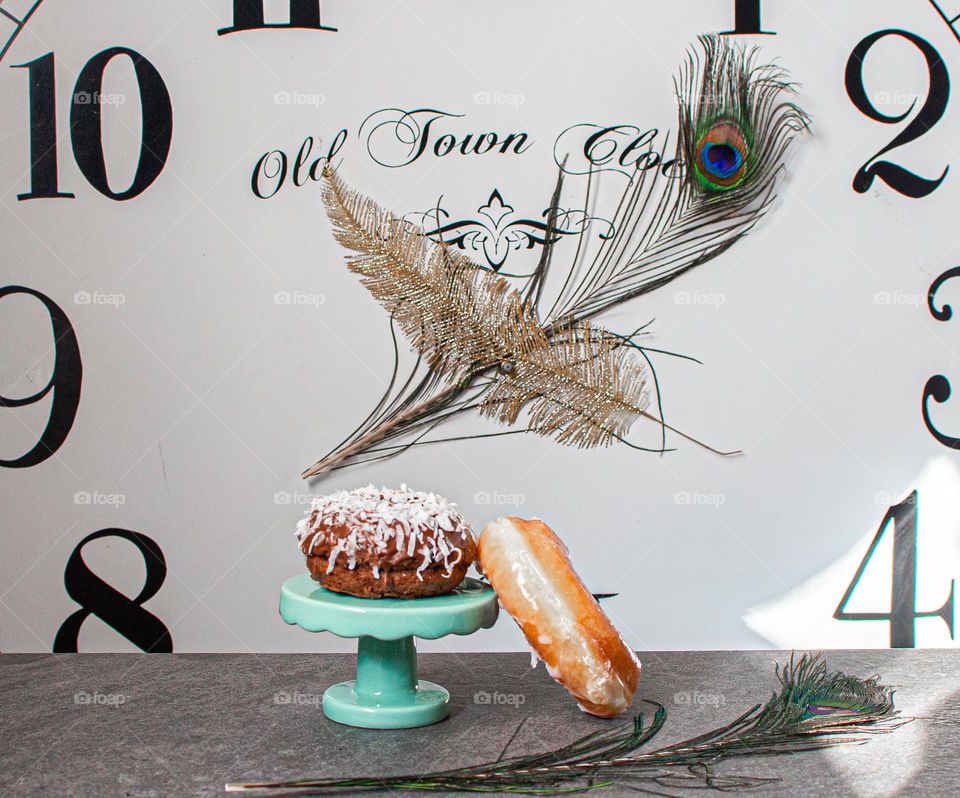 Two tasty doughnuts with a clock in the background and feathers 