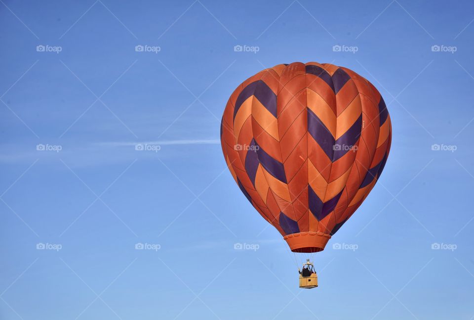 A hot air balloon festival in the winter creates a colorful scene. This balloon is flying and is orange.