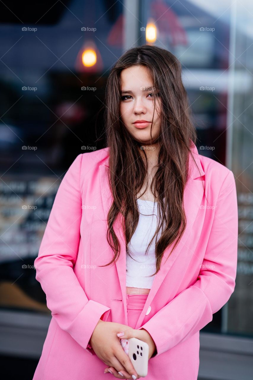 Beautiful young woman with long dark hair. Stylish outfit. Bright pink jacket. Street photoshot