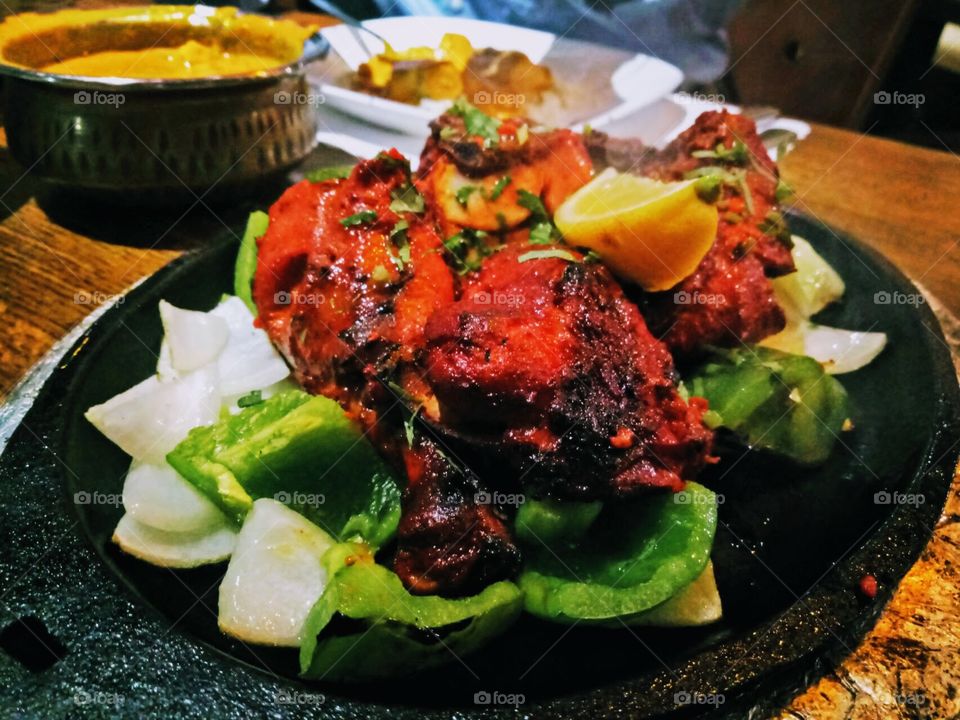 Chicken tandoori with green bell pepper, slice of white unions in a black sizzling plate. Tender and juicy, delicious dinner. Chicken curry on the other bowl. Indian food.