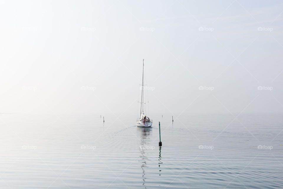 One lonely sailboat sailing off towards the fog on calm peaceful ocean 