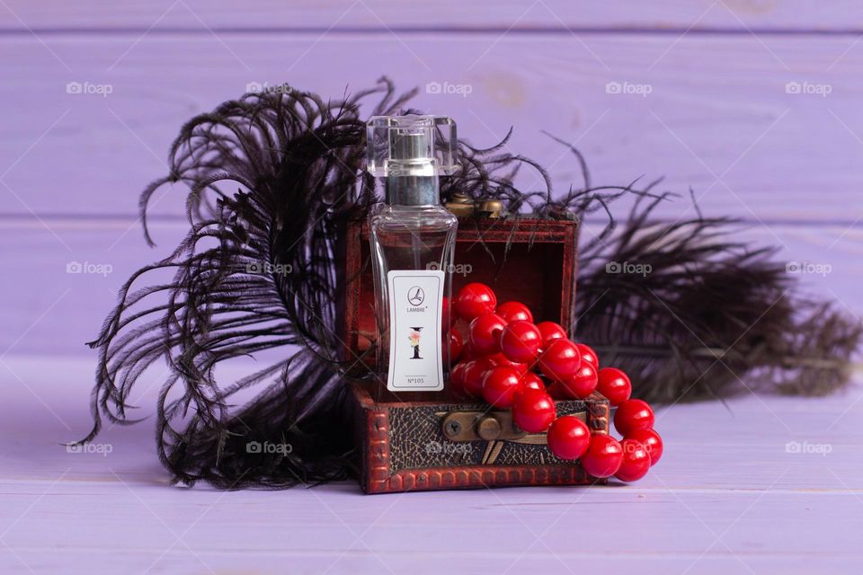 Aesthetic photo of parfum with black feathers, red necklaces and wooden box