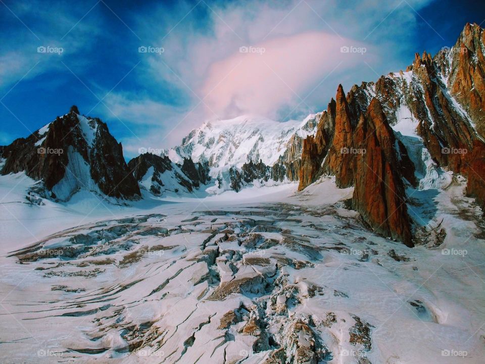 Close view of the Mer de Glace glacier with jagged mountains in the background and blue sky with pink tinted clouds