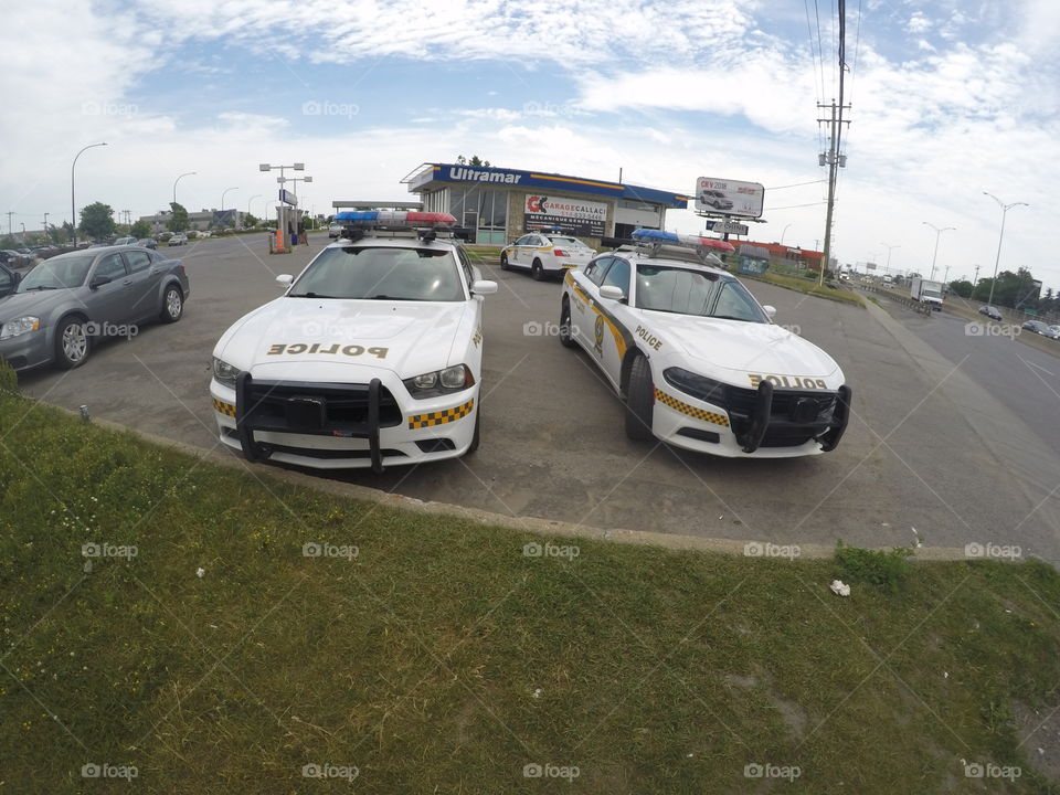 A picture of two Quebec provincial police cars parked in front of a gas station in Montreal. Dodge charger