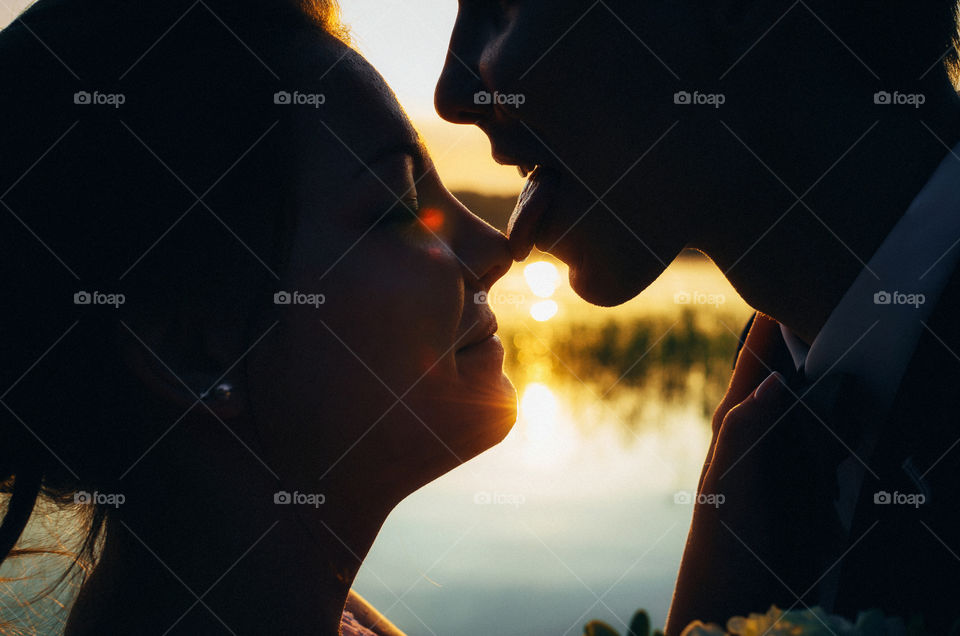 Silhouette of lovers look at each other at sunset light. Young man licks the nose of the girlfriend.