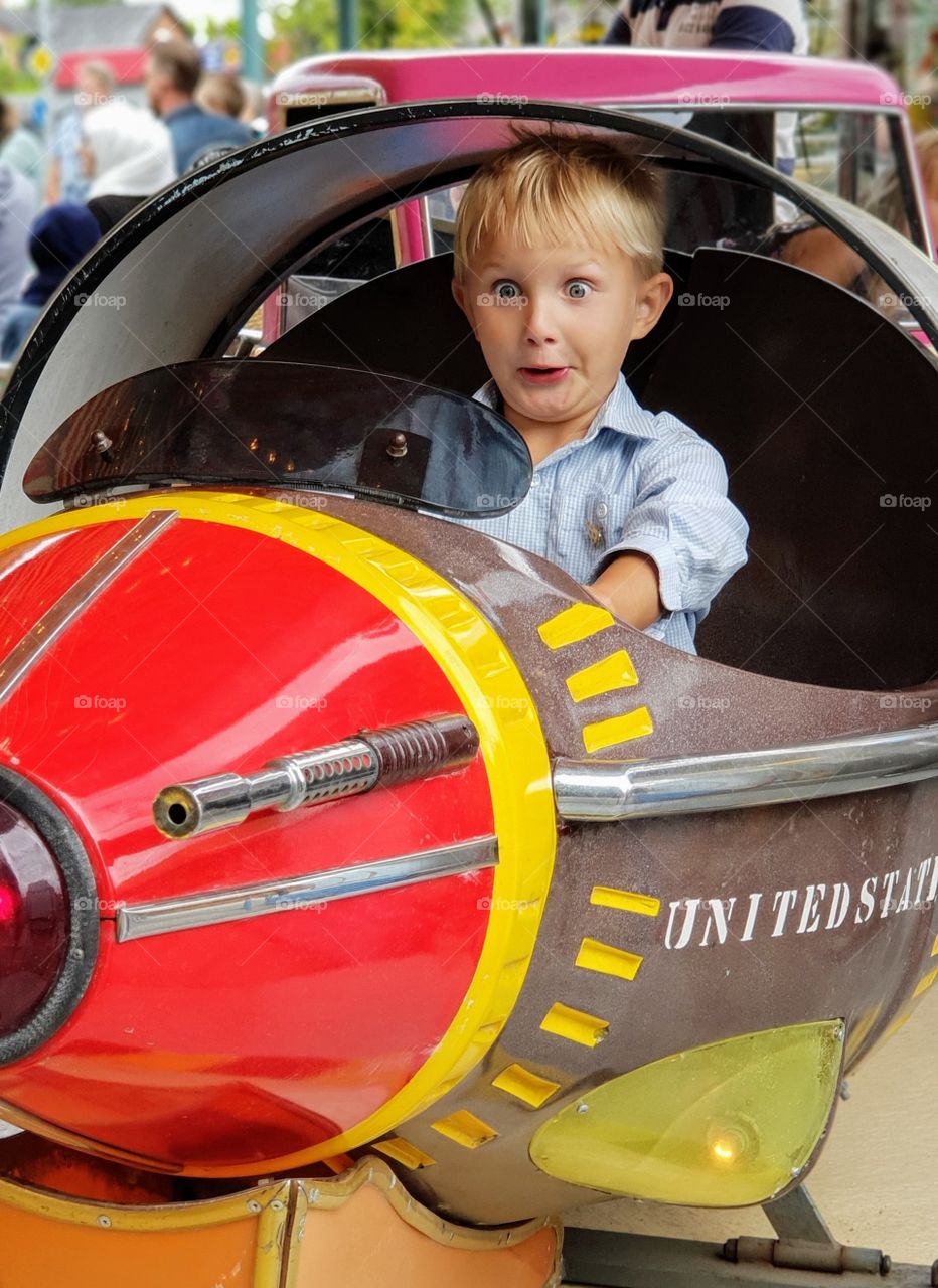 an excited boy riding a plane at an amusement park