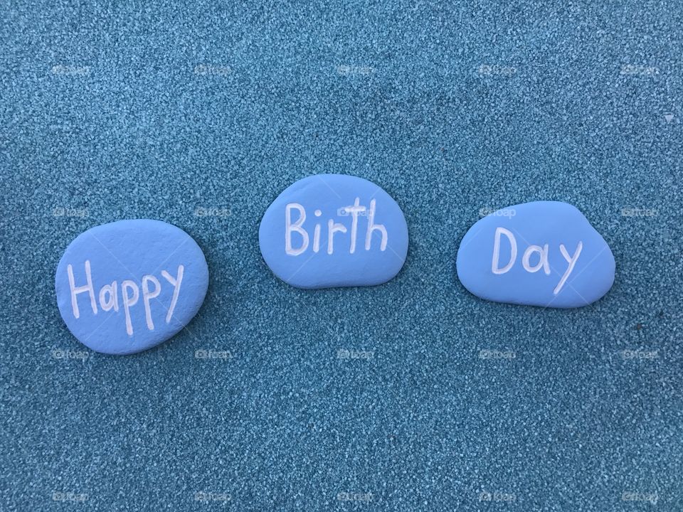 Happy Birthday message carved and colored on three stones over blue sand 