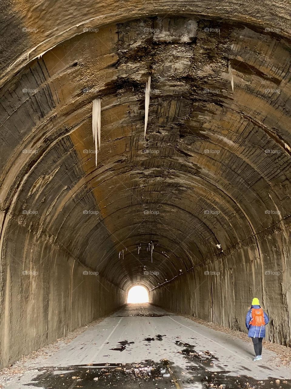 A person walking through an old railway tunnel with icicles hanging from the ceiling