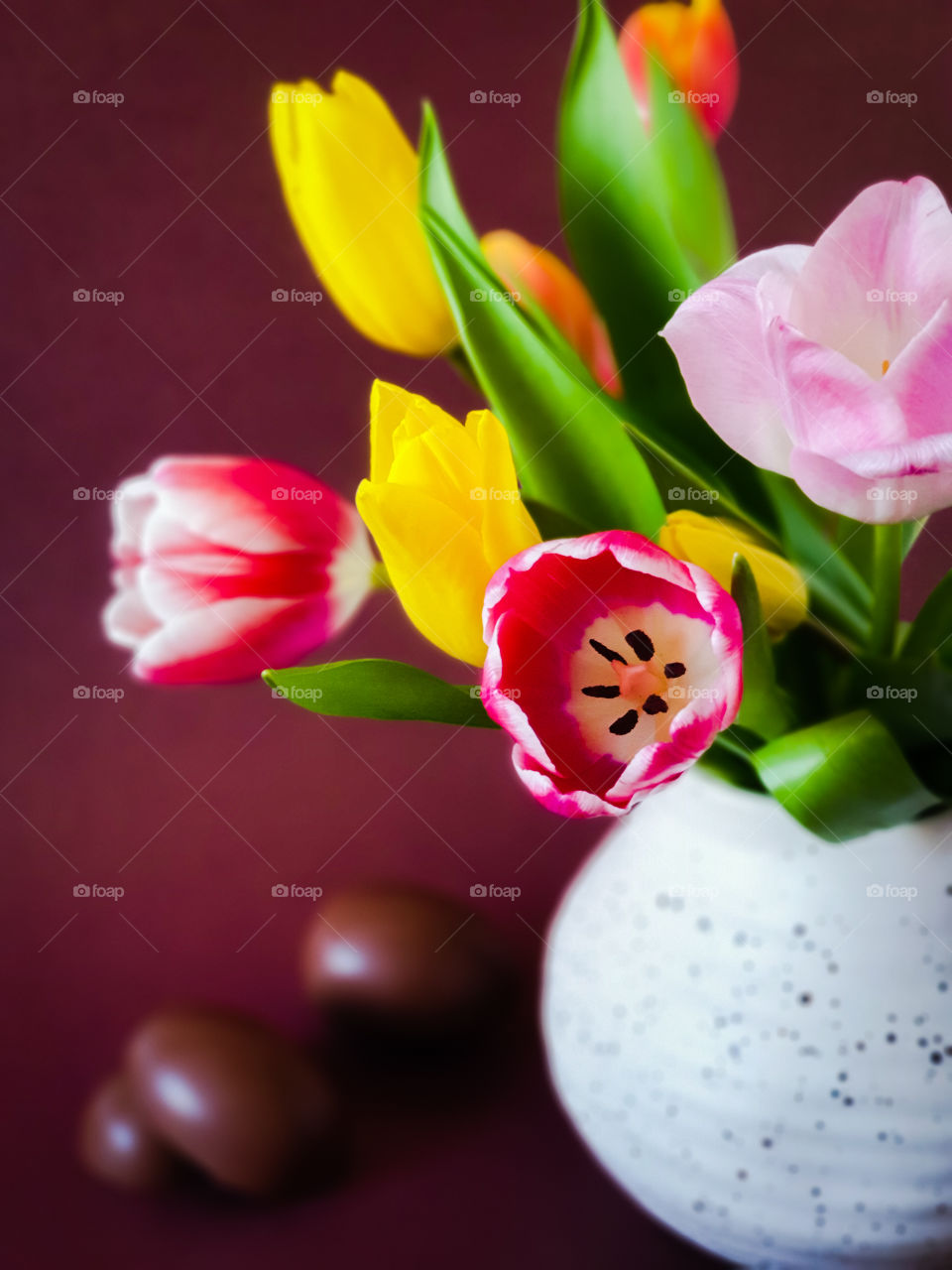 Spring bouquet.  Multi-colored tulips in a white clay jug with chocolate eggs on a brown background.  Easter holidays.  Horizontal orientation