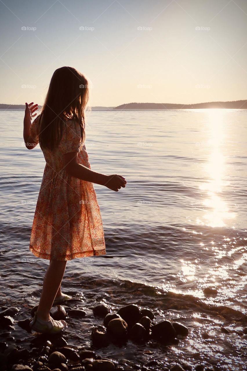 A young girl plays by the water’s edge as the summer sun sets over a beach in Washington State