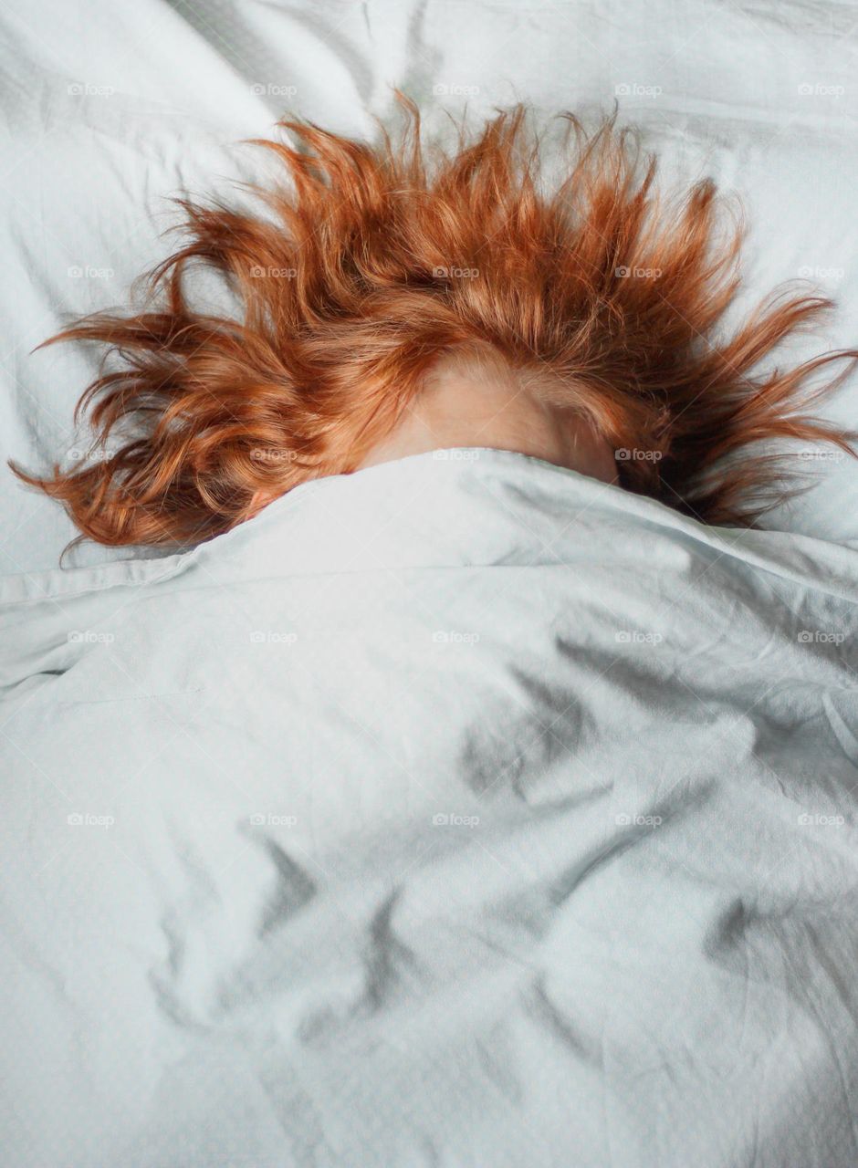 Woman hiding her face in the bed, red hair