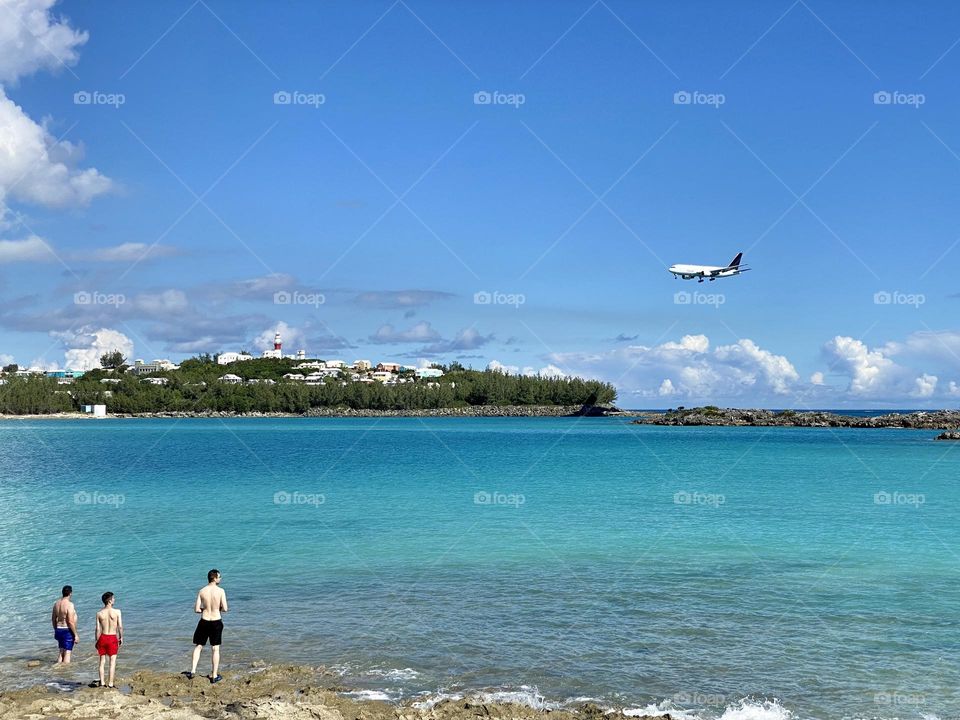 Three people watching a plane flying over a beach