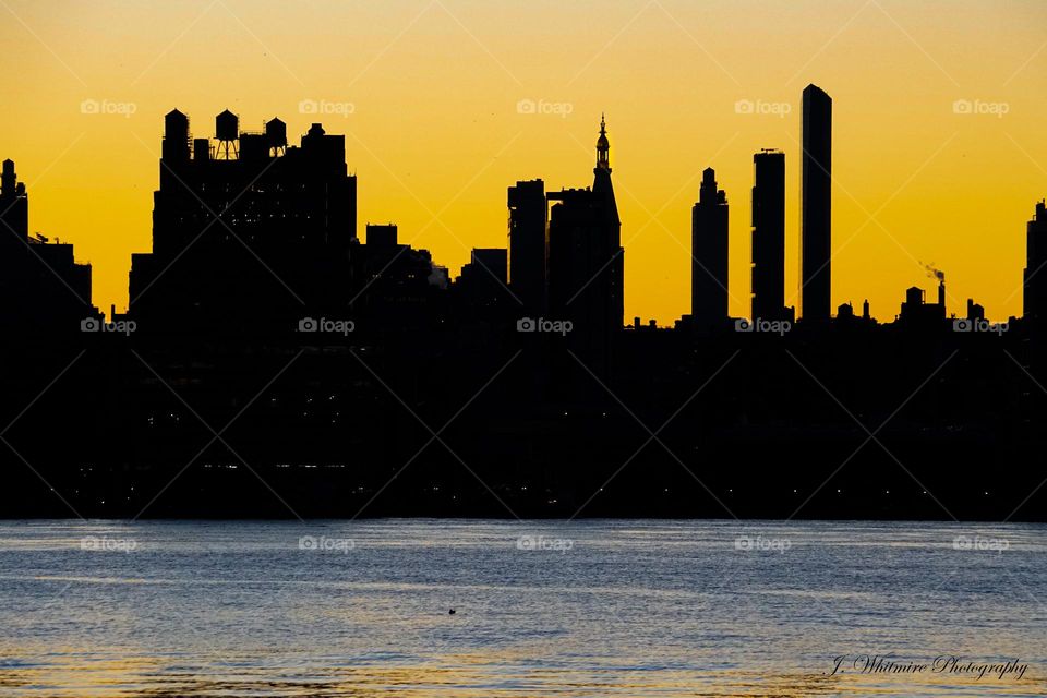 A part of the New York City skyline is backlit in bright yellow as the sun sets on a crisp fall evening