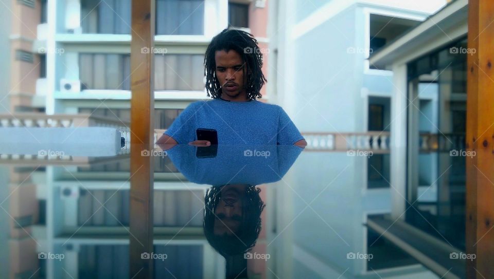 Reflection of a african man holding mobile phone on glass table
