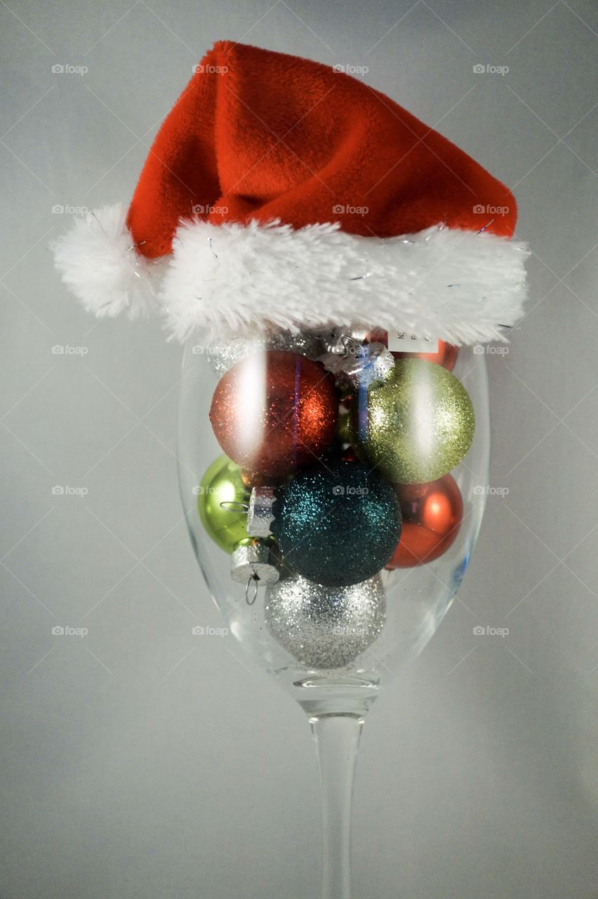 Sparkly Christmas ornaments in a wine glass with Santa hat on top