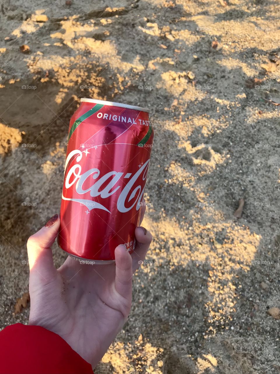 Holding a can of Coca Cola by the sand 