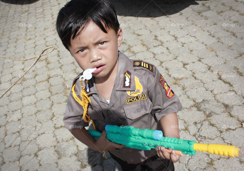 A little boy in police uniform with toy gun standing on street