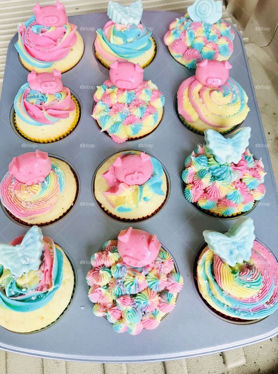 Beautiful delicious colorful pink, blue, and yellow cupcakes adorned with fun chocolate butterfly and pig molds. 