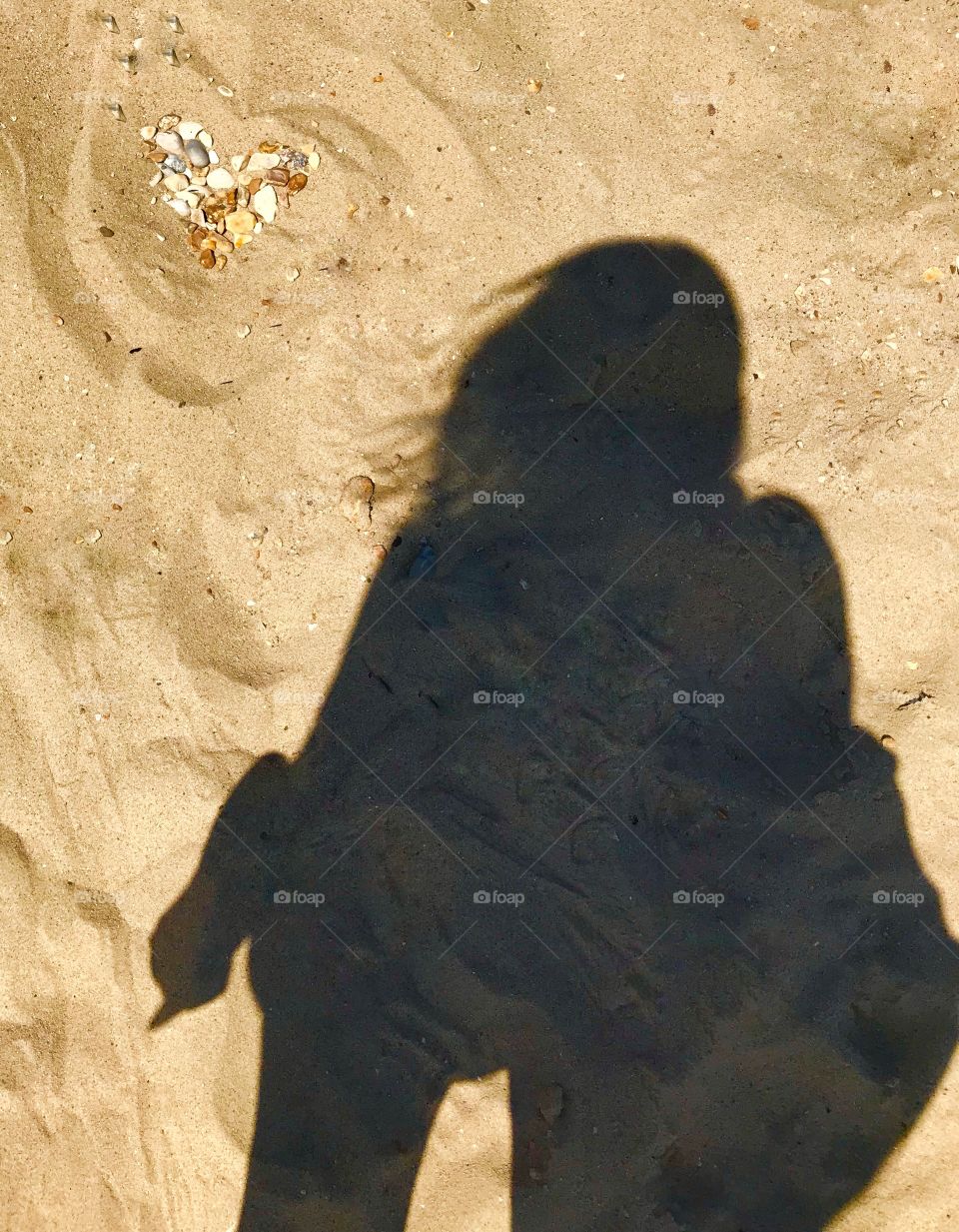 Heart in the sand and shadow of a girl. Sand sun shells pebbles. Pebble heart. Wind in hair. Contrast 