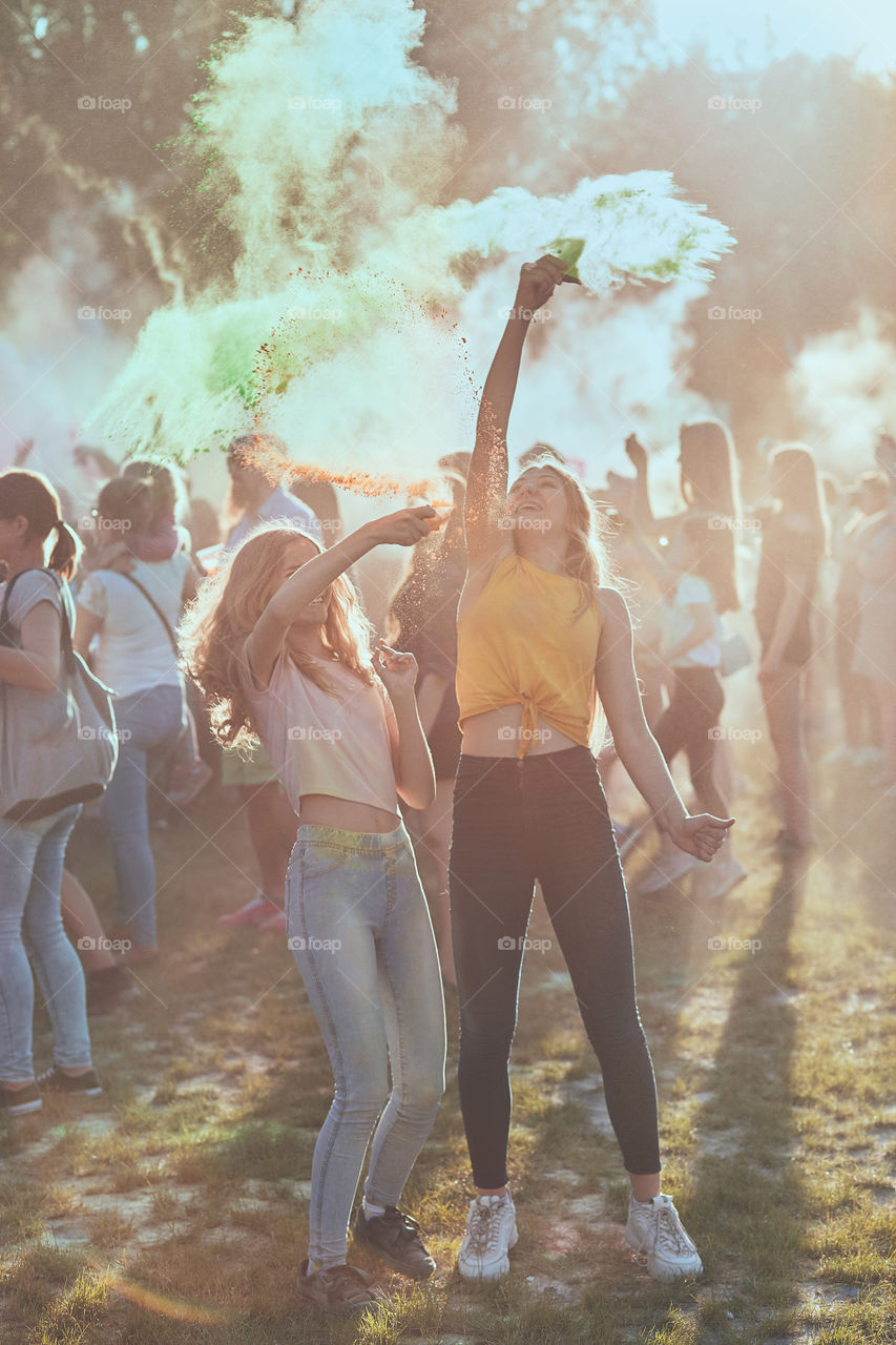 Portrait of happy smiling young girls with colorful paints on faces and clothes. Two friends spending time on holi color festival. Real people, authentic situations