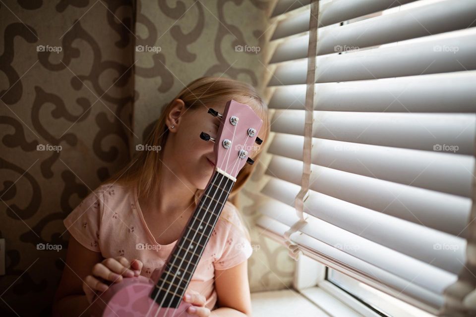 Little Caucasian girl playing on ukulele at home