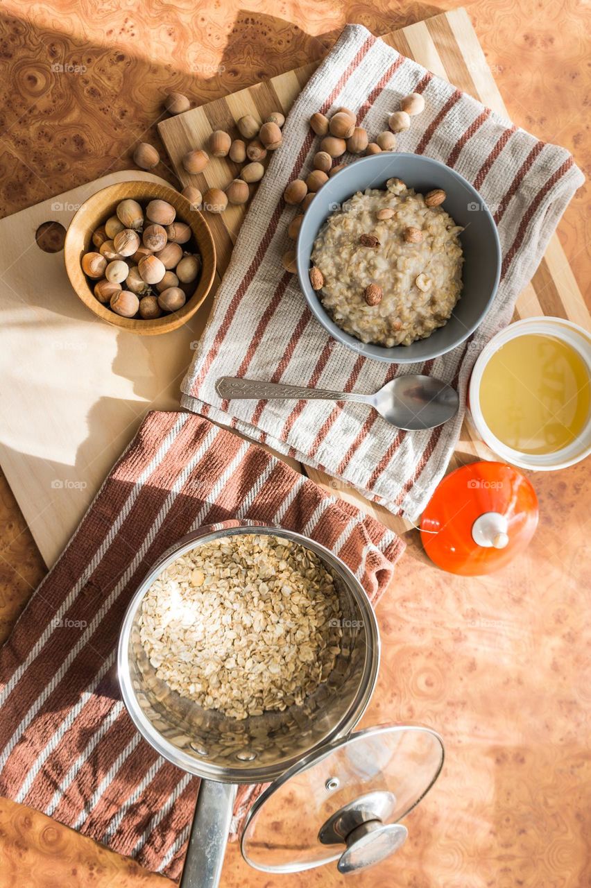 Cooked oatmeal in a deep gray plate with hazelnuts and honey.
