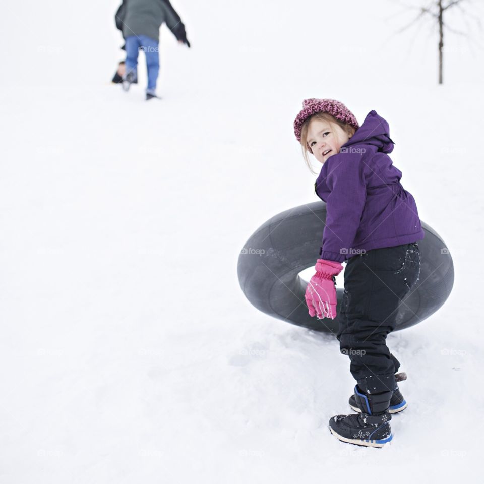 Girl hauling a sledding tube up a hill in the snow 