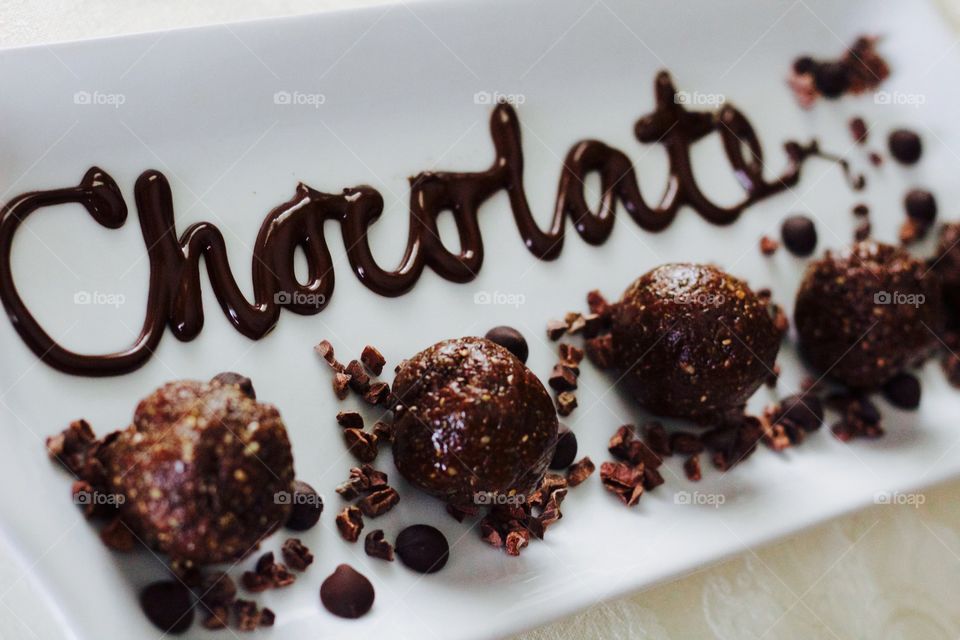 More Chocolate - Nut Butter Cocoa Bites on rectangular white dish with scattered cacao nibs and chocolate chips, and the word "Chocolate" written in chocolate drizzle